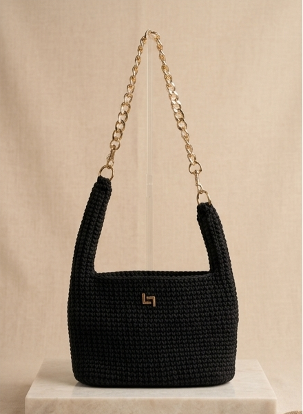 Black woven handbag with a gold chain strap on a beige background