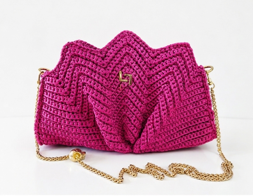Pink crocheted handbag with a gold chain on a white background