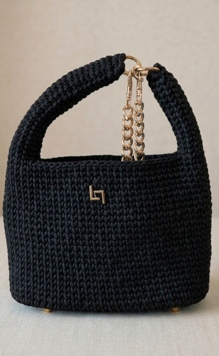 Black woven handbag with a gold chain handle on a light gray background